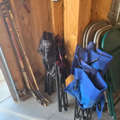 Sale Photo Thumbnail #79: Assorted folding camp chairs in blue and black, stored alongside vintage wooden hockey sticks and metal folding chairs in a garage.