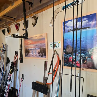 Sale Photo Thumbnail #90: Assorted garage and outdoor gear, including snow skis, fishing nets, a bow saw, mounted deer antlers, and framed beach-themed wall art.