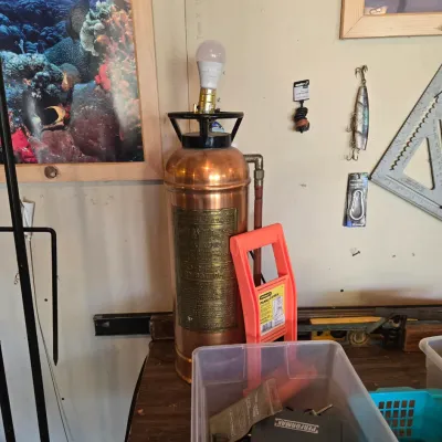 Sale Photo Thumbnail #91: Vintage Dayton copper and brass fire extinguisher converted into a novelty table lamp, displayed alongside workshop tools and fishing gear.