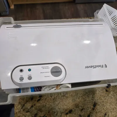 Sale Photo Thumbnail #73: White FoodSaver vacuum sealer machine with control dial and buttons, stored in a clear plastic bin.