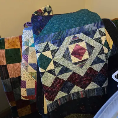 Sale Photo Thumbnail #27: A collection of handmade quilts in various geometric patterns and colors, draped over a wooden quilt rack.