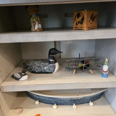 Sale Photo Thumbnail #42: Assorted rustic shelf decor, including wooden loon decoys, a metal biplane model, a small boat-shaped wall shelf, and various figurines.