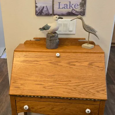 Sale Photo Thumbnail #56: Oak slant-front secretary desk with cabriole legs and white ceramic knobs, topped with decorative bird figurines and a hanging "Welcome to the Lake" sign.
