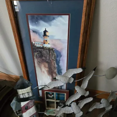 Sale Photo Thumbnail #62: Nautical-themed decor collection featuring a framed lighthouse print in a wooden frame, a painted metal lighthouse sculpture, and a metal seagull wall hanging.
