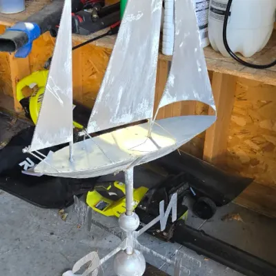 Sale Photo Thumbnail #95: Vintage metal sailboat weather vane with directional indicators, mounted on a wooden base.