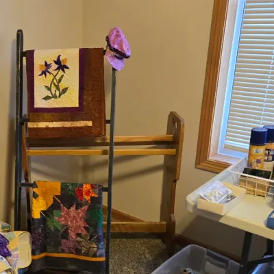 Sale Photo Thumbnail #28: Two wooden quilt display racks, one ladder-style and one floor-standing, shown with handmade quilts and sewing supplies.