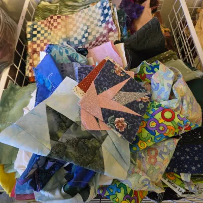 Assorted quilting fabric scraps and partially completed quilt blocks in a white wire storage basket.