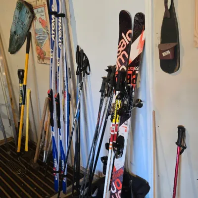 Sale Photo Thumbnail #88: Assorted winter sports gear including Atomic and Salomon downhill skis, ski poles, boots, and a single red trekking pole.