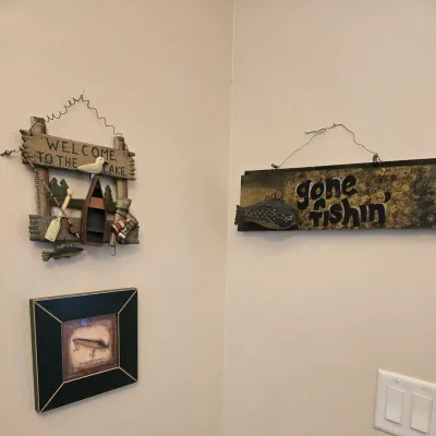 Sale Photo Thumbnail #60: Rustic cabin-style wall decor including a "Welcome to the Lake" sign with a miniature canoe, a "gone fishin'" sign, and a small framed print of a fishing lure.