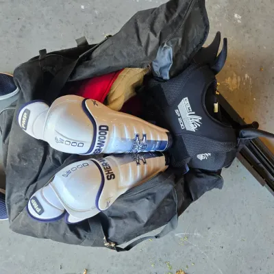 Sale Photo Thumbnail #97: Sher-Wood PMP 3000 shin guards and CCM SP 200 shoulder pads inside a black zippered hockey gear bag.