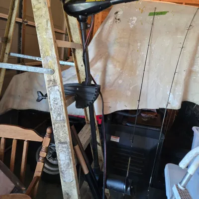 Sale Photo Thumbnail #77: Minn Kota electric trolling motor mounted to a wooden stepladder, shown alongside fishing rods in a garage setting.