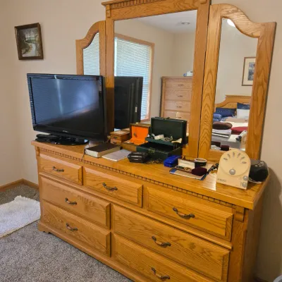 Sale Photo Thumbnail #52: Traditional oak triple-mirror dresser featuring nine drawers with brass-toned pulls and dentil molding details, shown holding a television and various personal items.
