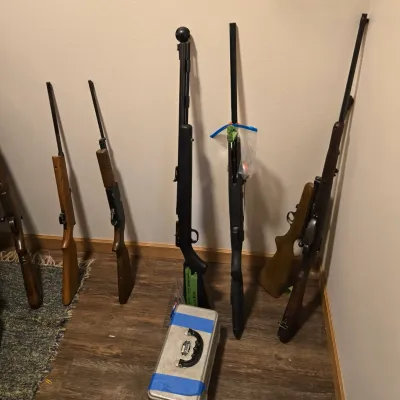 Collection of vintage and modern long guns, including rifles and shotguns with wood and synthetic stocks, displayed alongside a metal...