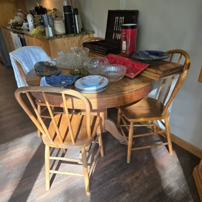 Sale Photo Thumbnail #51: Round oak pedestal dining table with three matching spindle-back chairs, displaying various glassware, plates, and a flatware chest.