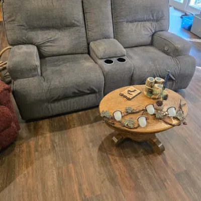 Sale Photo Thumbnail #46: Contemporary grey fabric power reclining loveseat with a center console and cup holders, paired with a round oak coffee table featuring a pedestal base.