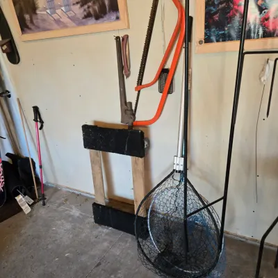 Sale Photo Thumbnail #89: Assorted outdoor and utility gear, including a large fishing net, a bow saw with an orange frame, a pipe wrench, and a wooden stand.