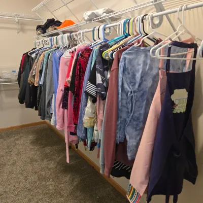 Sale Photo Thumbnail #63: Assorted men's and women's clothing, including shirts, sweaters, and jackets, hanging on a wire closet rack.