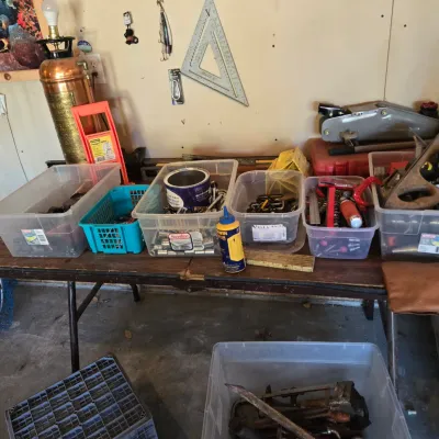 Sale Photo Thumbnail #92: Assorted workshop tools and hardware organized in plastic storage bins on a folding table, including hand tools, sockets, and a vintage copper fire extinguisher lamp.