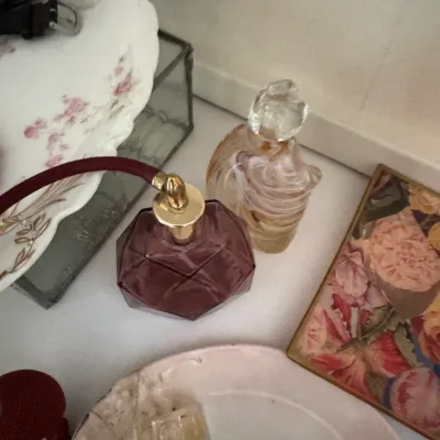 Sale Photo Thumbnail #178: Vintage vanity collection featuring a geometric purple glass perfume bottle with an atomizer, an art glass perfume bottle with a swirl design, and decorative floral plates.