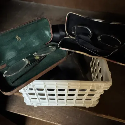 Sale Photo Thumbnail #110: Two pairs of eyeglasses in their respective cases, including a vintage Polo Ralph Lauren case with green velvet lining, resting on a small white plastic basket.