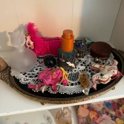 Sale Photo Thumbnail #193: Assorted vintage vanity items, including a frosted glass perfume bottle, small fabric elephant figurines, and a decorative bottle on a brass-rimmed mirrored tray.