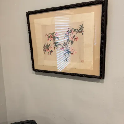 Sale Photo Thumbnail #142: Framed Asian-style watercolor painting depicting pink cherry blossoms on a branch, set in a dark carved wooden frame with a beige mat.