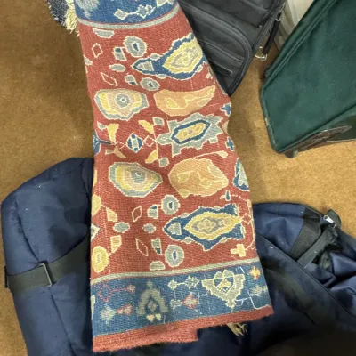 Sale Photo Thumbnail #113: Rolled-up Persian or Turkish style area rug featuring geometric patterns in red, blue, and gold tones, shown alongside various travel bags.