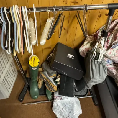 Sale Photo Thumbnail #158: Adjustable metal garment rack holding various plastic and padded hangers, with a selection of winter boots, a Sorel shoebox, and a plastic bag stored on the bottom shelf.