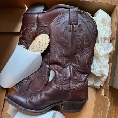 Sale Photo Thumbnail #53: Pair of vintage brown leather cowboy boots with decorative stitching, stored in their original cardboard box with packing materials.