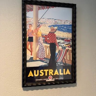 Sale Photo Thumbnail #64: Framed vintage-style Australia travel poster depicting a beach scene with figures in 1930s attire, housed in a dark, textured frame.