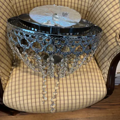 Sale Photo Thumbnail #269: Modern chrome flush-mount ceiling light fixture featuring an ornate filigree band and hanging crystal bead strands, resting on a plaid armchair.
