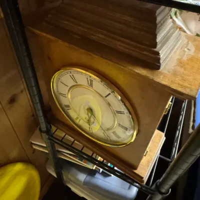 Sale Photo Thumbnail #157: Vintage wooden mantel clock with a brass-rimmed face and Roman numerals, displayed on a wire shelf.