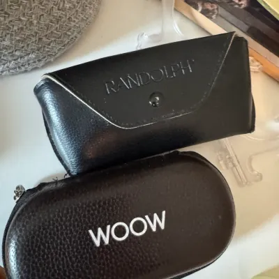 Sale Photo Thumbnail #221: Two black eyewear cases, including a snap-closure Randolph case and a zippered Woow case, showing light wear.