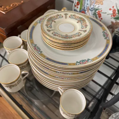 Sale Photo Thumbnail #343: Vintage porcelain dinnerware set featuring a stack of dinner plates, matching saucers, and several teacups with gold-trimmed rims and ornate floral borders.