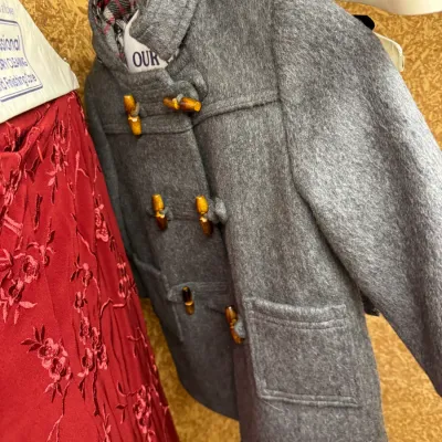 Sale Photo Thumbnail #94: Vintage children's grey wool duffle coat with wooden toggle closures and a plaid-lined hood, hanging next to a red embroidered garment.