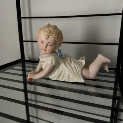 Sale Photo Thumbnail #349: Vintage bisque porcelain piano baby figurine, depicting a crawling child in a white dress with a blue bow, in good condition.