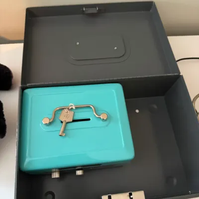Sale Photo Thumbnail #227: Two metal cash boxes, featuring a smaller turquoise box with a key nested inside a larger dark gray lockbox.