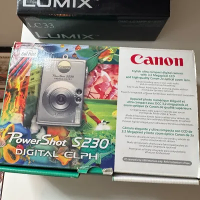 Sale Photo Thumbnail #225: Vintage digital cameras in their original packaging, including a Canon PowerShot S230 Digital Elph and a Panasonic Lumix LC33, circa early 2000s.