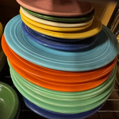 Sale Photo Thumbnail #7: Stack of vintage Fiesta ceramic plates and platters in a variety of colorful glazes, including turquoise, orange, green, and yellow.
