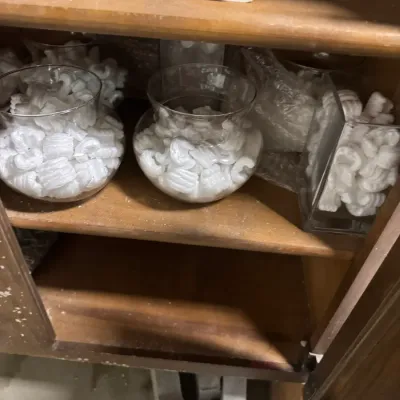 Sale Photo Thumbnail #104: Assorted clear glass vases and containers filled with white foam packing peanuts, displayed on wooden shelves.