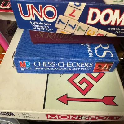 Sale Photo Thumbnail #118: Stack of vintage board games including Monopoly, Milton Bradley Chess and Checkers, Scrabble, and Uno Dominoes, showing some shelf wear on the boxes.
