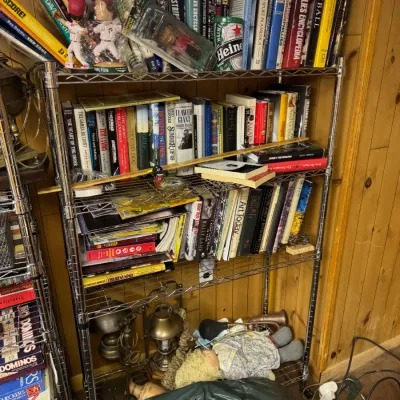 Sale Photo Thumbnail #129: Four-tier wire shelving unit filled with books, sports memorabilia, vintage dolls, and brass lamps.