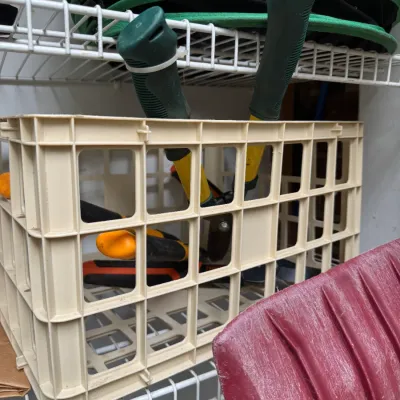 Sale Photo Thumbnail #70: Assorted garden tools, including loppers with yellow and green handles, stored inside a beige plastic crate on a wire shelf.