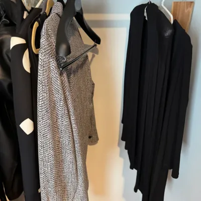 Sale Photo Thumbnail #160: Assorted women's outerwear and tops hanging in a closet, including a black and white patterned jacket and a long black cardigan.