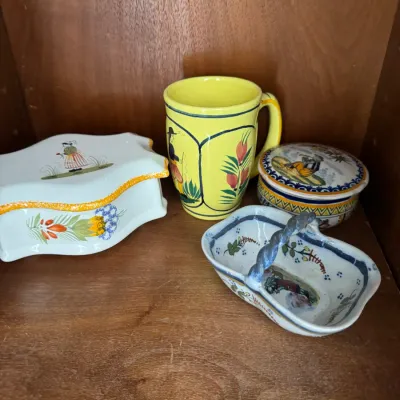 Sale Photo Thumbnail #284: Collection of French Quimper-style hand-painted pottery, including a yellow mug, a small lidded box, a shaped trinket dish, and a miniature basket with a twisted handle.