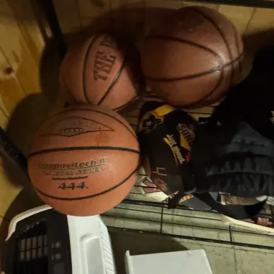 Sale Photo Thumbnail #146: Assorted used basketballs, including a Baden Compositech II 444 indoor/outdoor basketball, stored on a wire shelf.