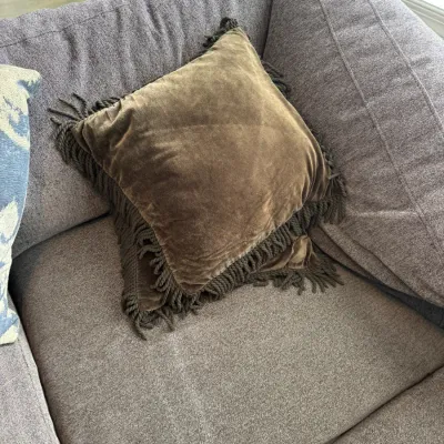 Sale Photo Thumbnail #316: Square brown velvet throw pillow featuring a thick, twisted rope fringe border, shown resting on a gray upholstered sofa.