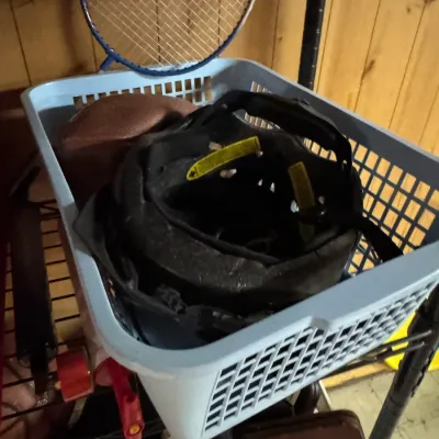 Sale Photo Thumbnail #148: Light blue plastic basket containing a black helmet, a football, and a badminton racket, resting on a wire shelf.