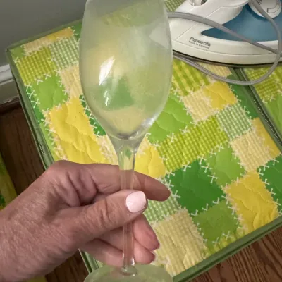 Sale Photo Thumbnail #325: Frosted glass wine goblet with a clear stem, held in hand, shown alongside a Rowenta steam iron.