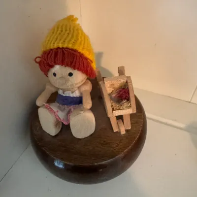 Sale Photo Thumbnail #195: Vintage wooden music box featuring a small doll with a yellow knit hat sitting next to a miniature wheelbarrow.